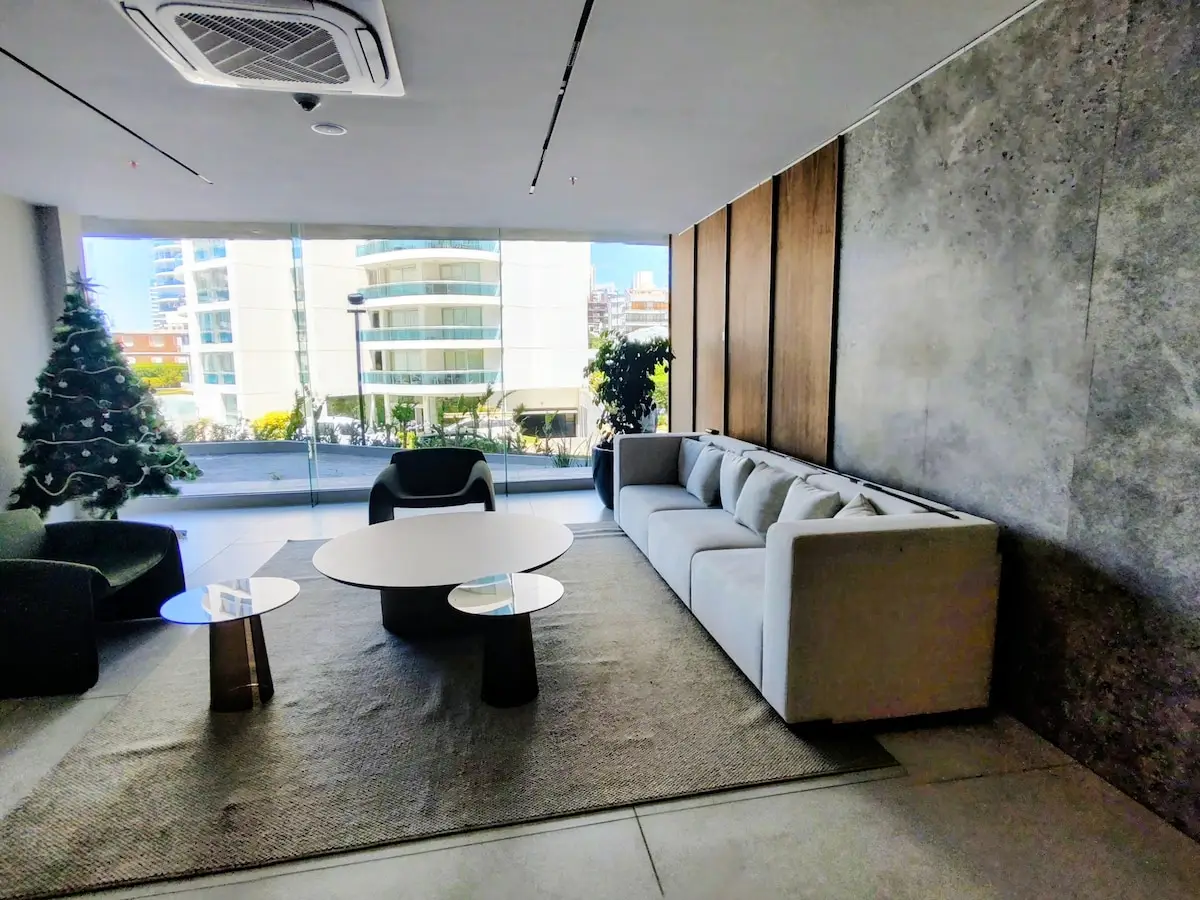 Recepción del edificio con área de espera de estética minimalista, hormigón visto y grandes ventanales.